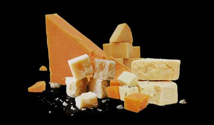 A selection of cheeses with a bunch of red grapes.