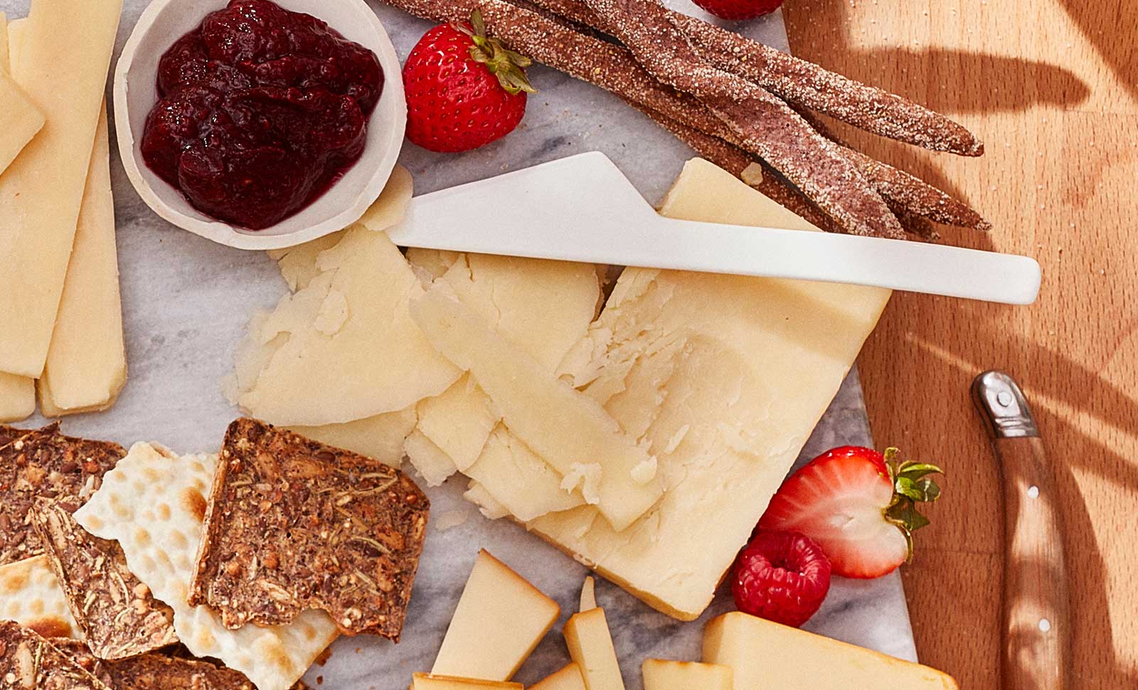 Two-year naturally aged cheddar cut with a knife served with multigrain crackers and strawberries.