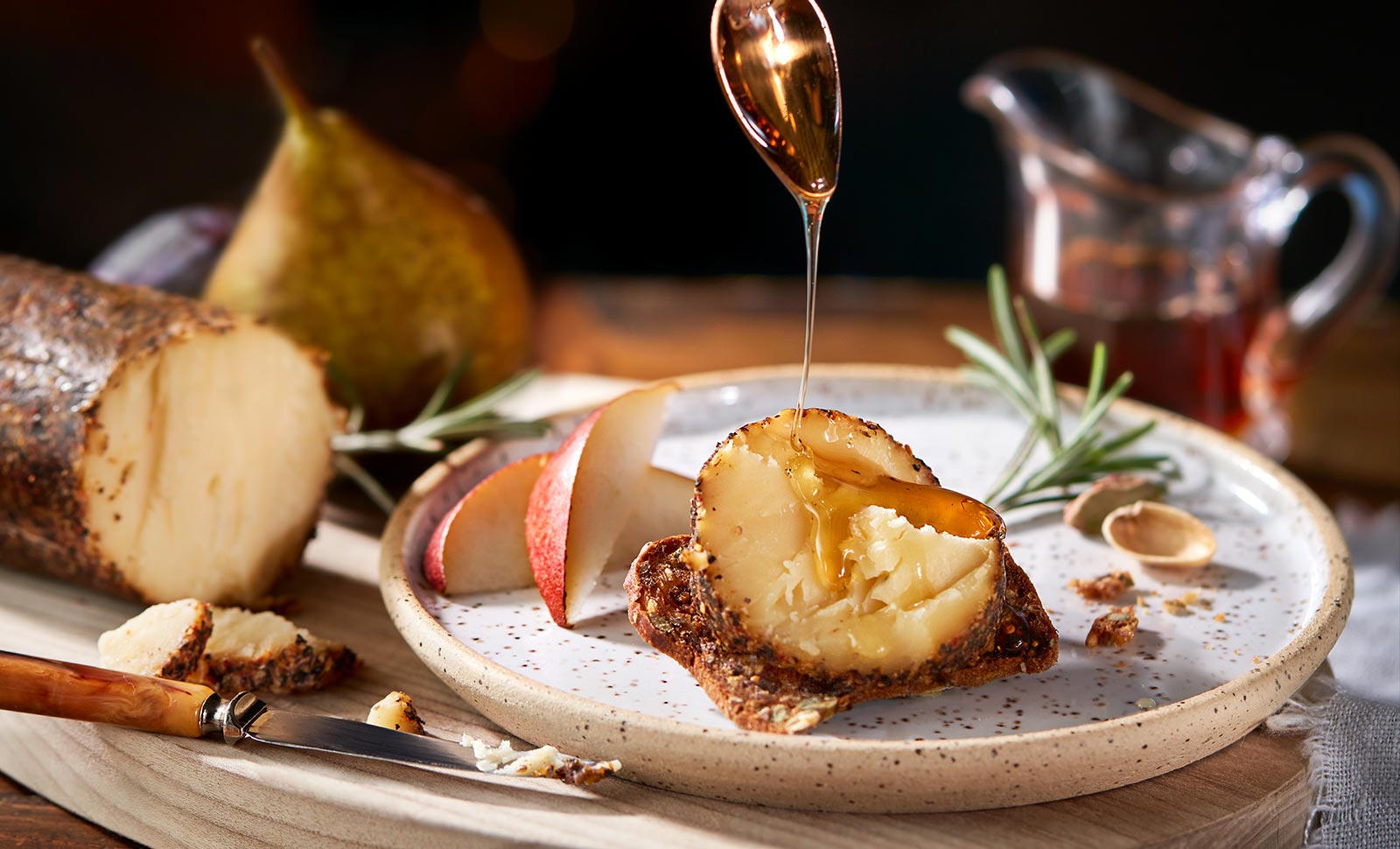 A piece of maple cheddar with cracked pepper cheese log on a plate being drizzled with honey.