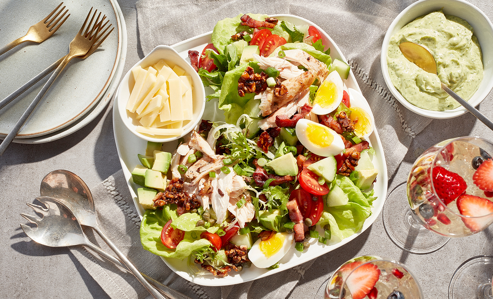 A colorful brunch salad made of mixed greens, sliced eggs, avocado cubes, tomatoes with a small bowl of sliced cheese.