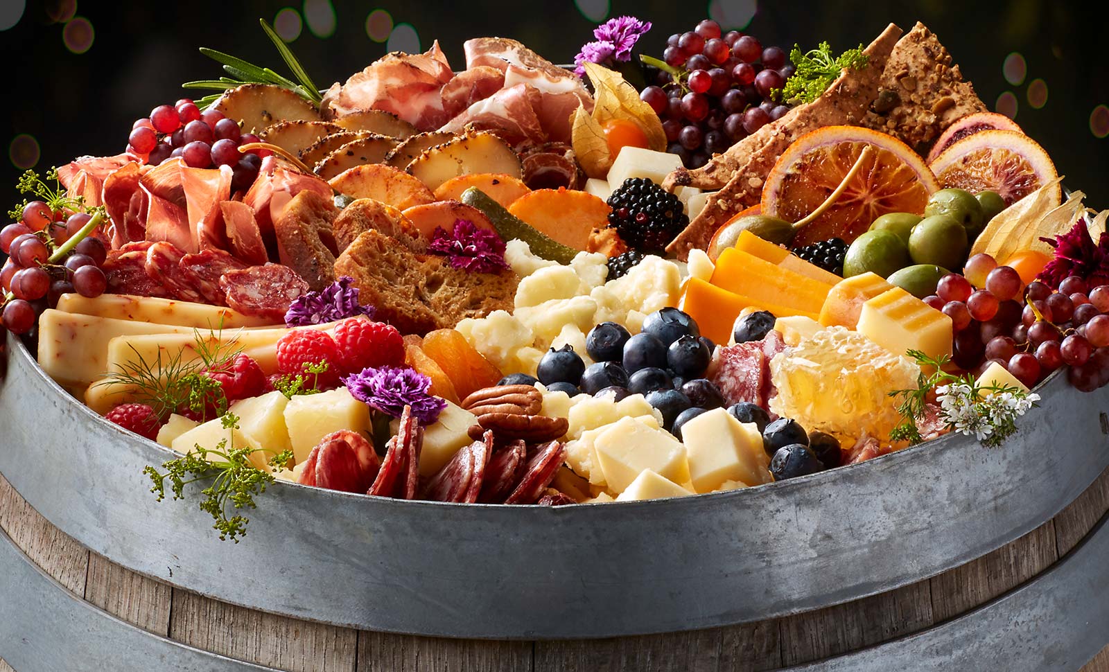 A wooden barrel topped with an assortment of cheeses, meats, fruits and breads.