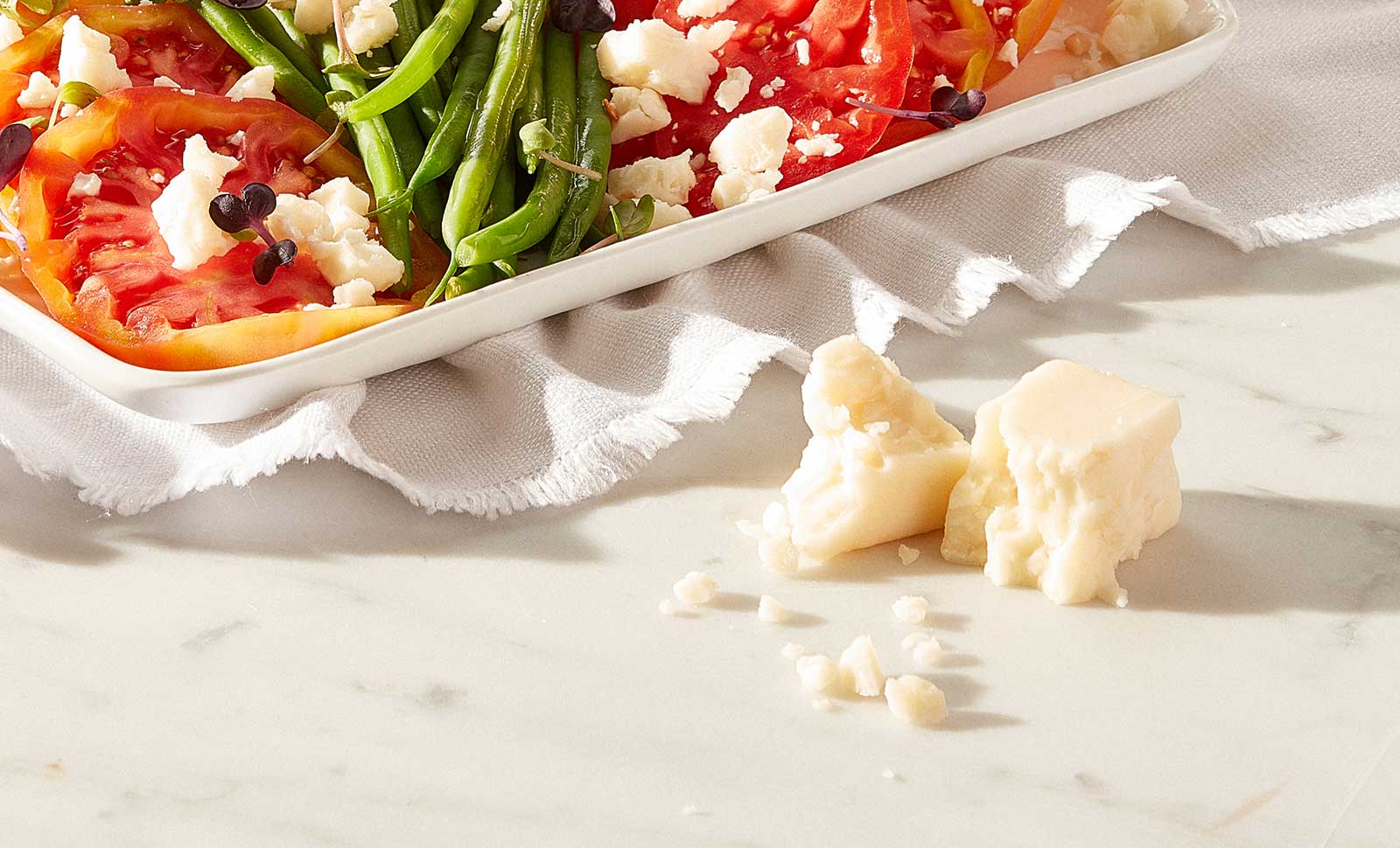 Two broken pieces of artisan goat cheddar cheese next to a plate of mixed vegetables.