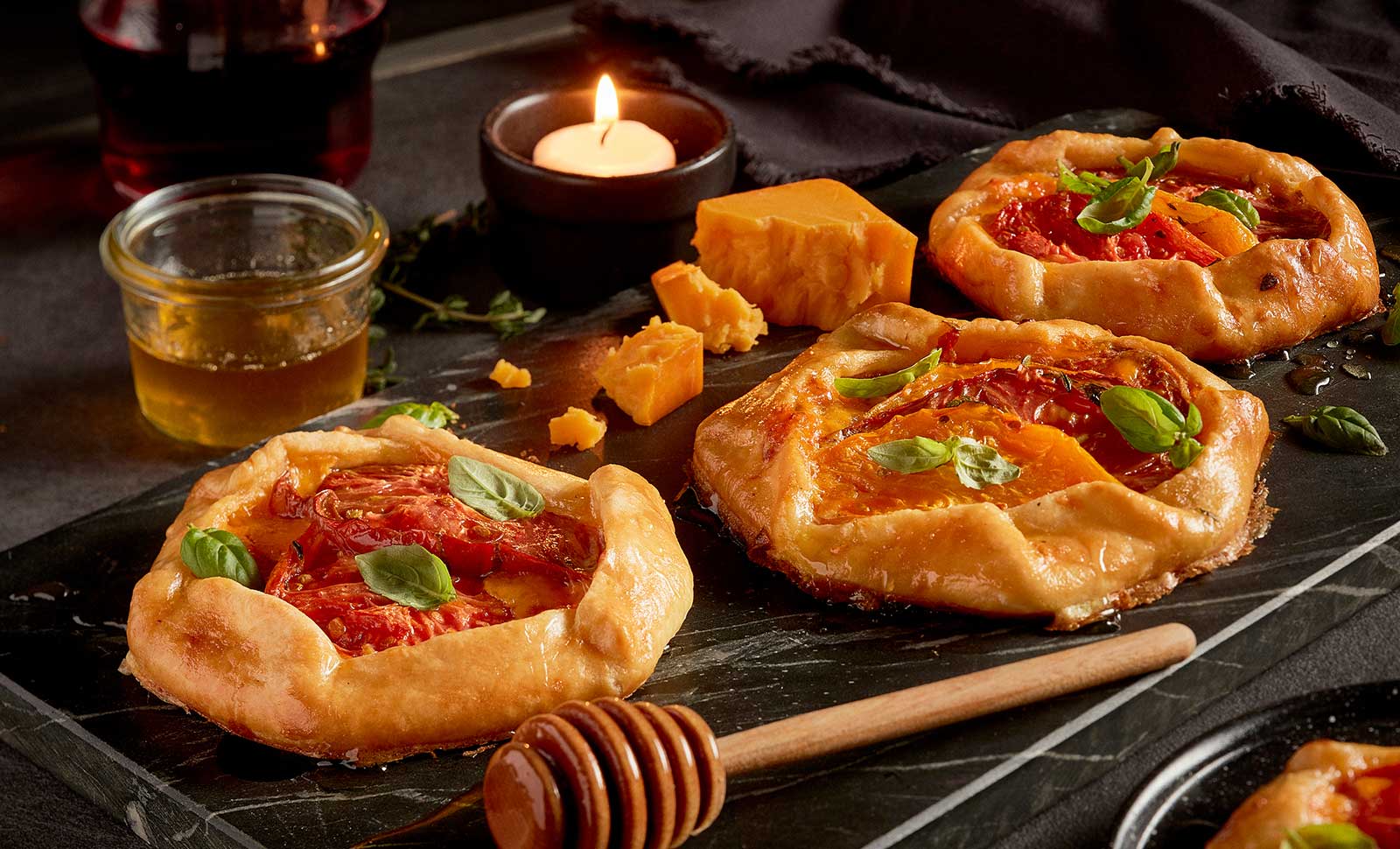 Three mini tomato cheese galettes with lavender honey along with pieces of cheddar cheese.
