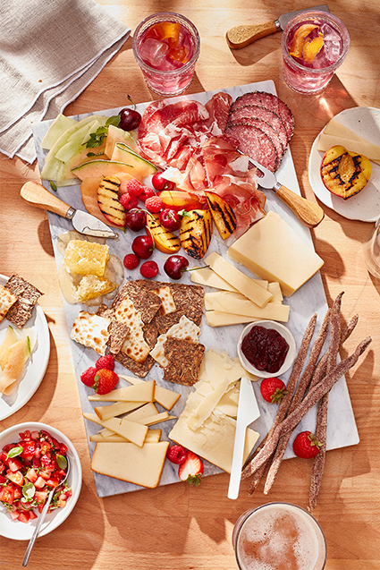 A summer inspired charcuterie board with aged cheddars, slices of salami and prosciutto, crackers, raspberries and cherries.
