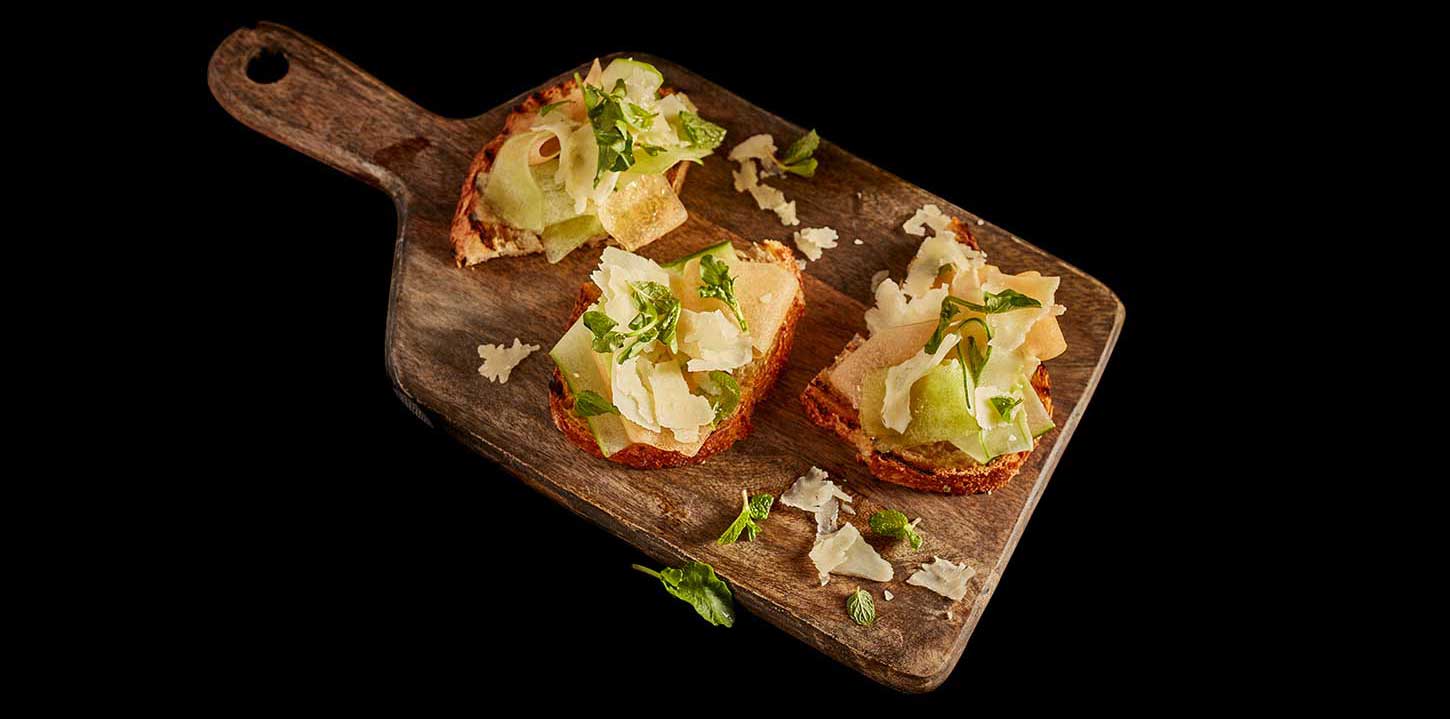 Three servings of cucumber melon caprese crostinis served on a wooden serving platter.