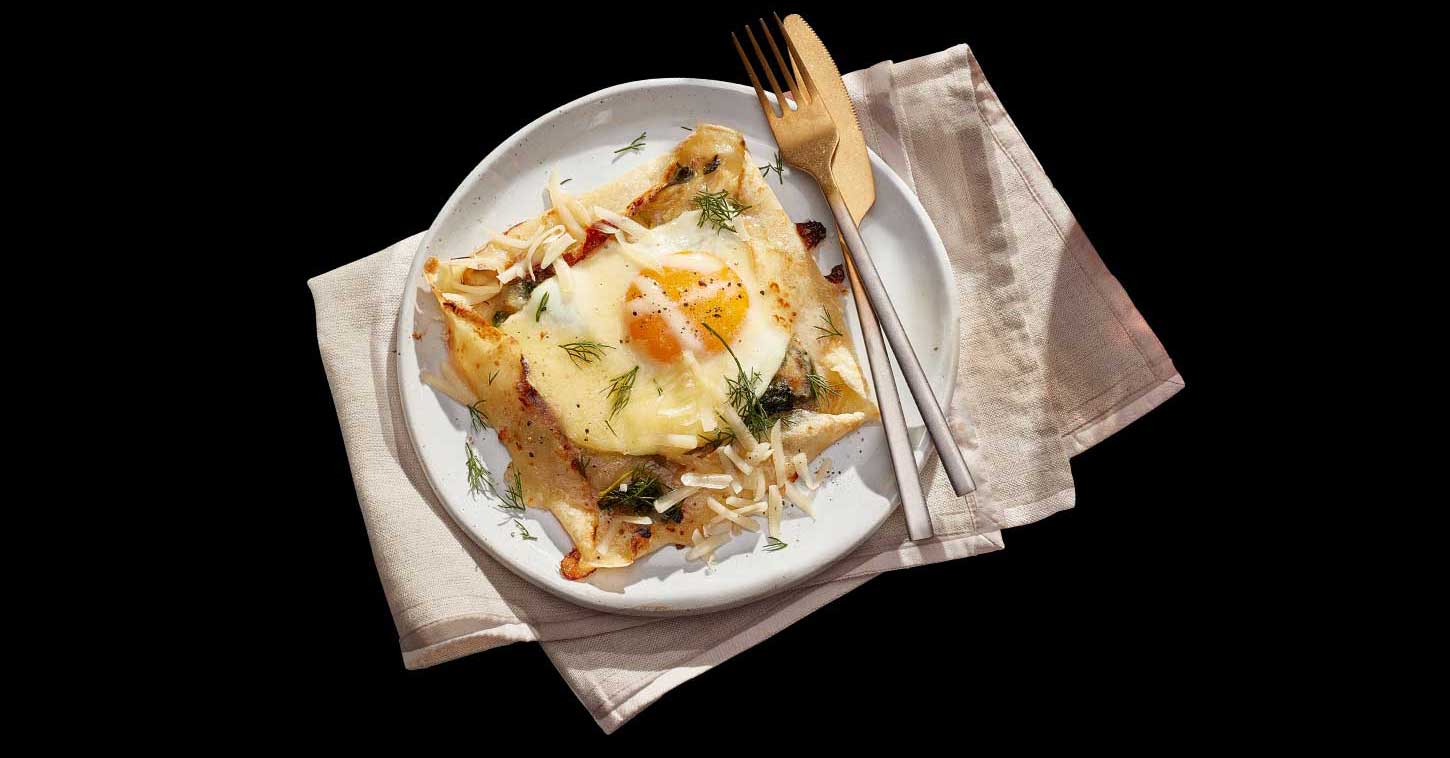Open faced savoury cheddar herbs crepes on plate with a fork and knife.