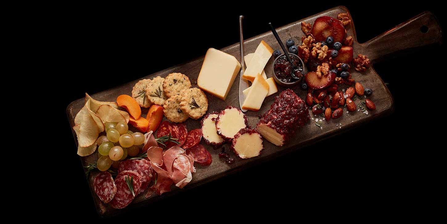 A fall-inspired charcuterie board with a cheddar cheese log, smoke cheddar cheese, jam, grapes, slice salami, biscuits, almonds, blueberries and walnuts.