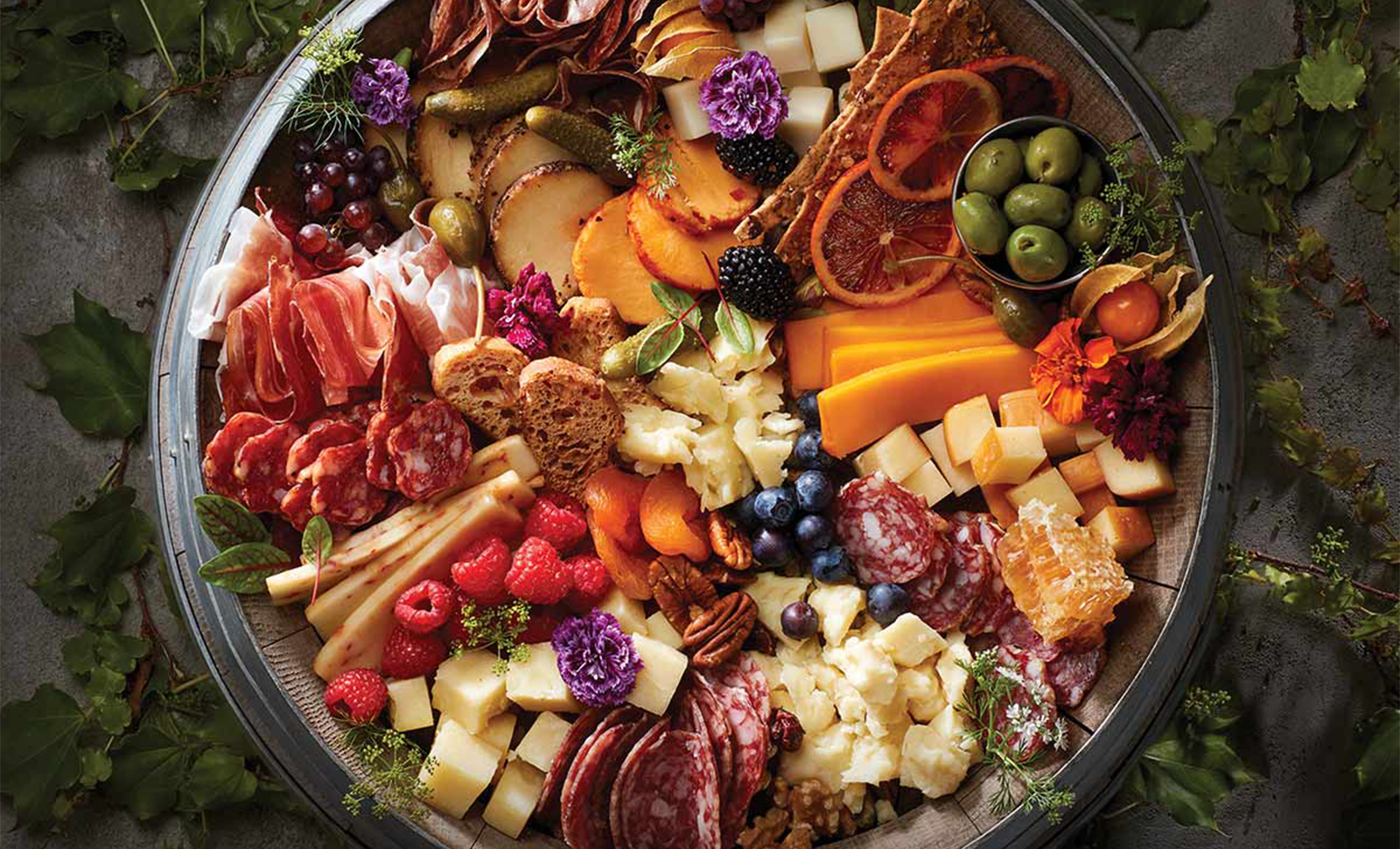 A wooden barrel topped with an assortment of cheeses, meats, fruits and breads
