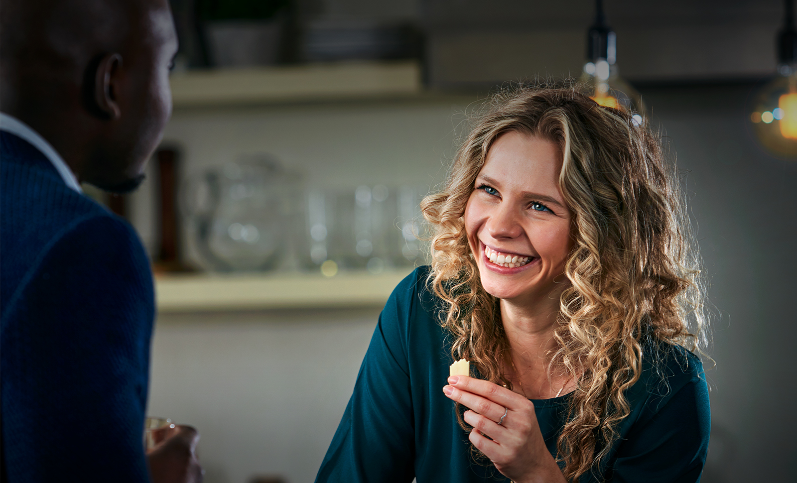 A woman at a kitchen party enjoying cheese while talking with a man.