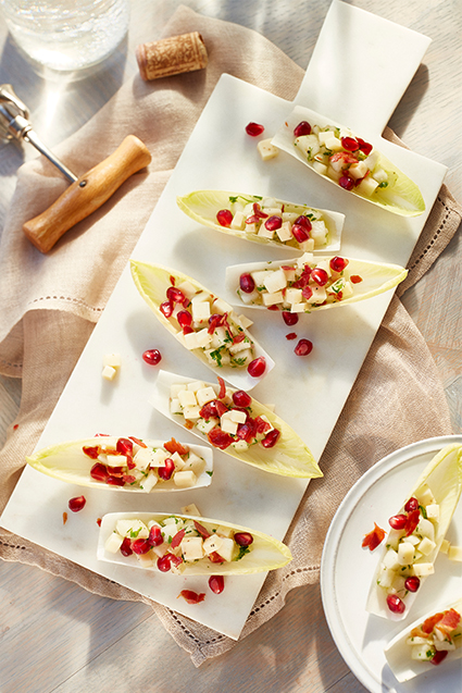 Seven pieces of endive leaves pear salad on a white plate served with a glass of white wine.