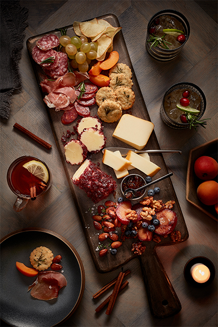 A fall inspired charcuterie board filled with slices naturally aged cheddar, cheddar logs, almonds, raspberries, blueberries, variety of sliced meats, grapes and biscuits.