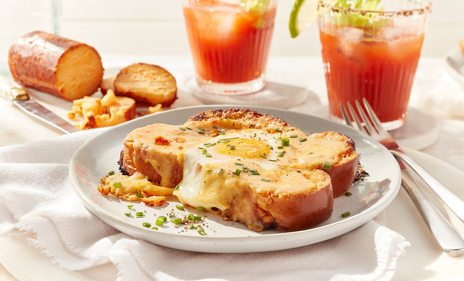 Savoury French toast chipotle bechamel on a plate in front of a chipotle cheddar cheese log and two glasses of clamato juice.