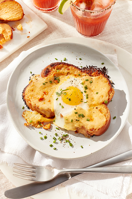 Savoury French toast chipotle bechamel on a plate in front of a chipotle cheddar cheese log and two glasses of clamato juice.
